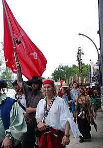 The pirates parade into the fort behind their flag.